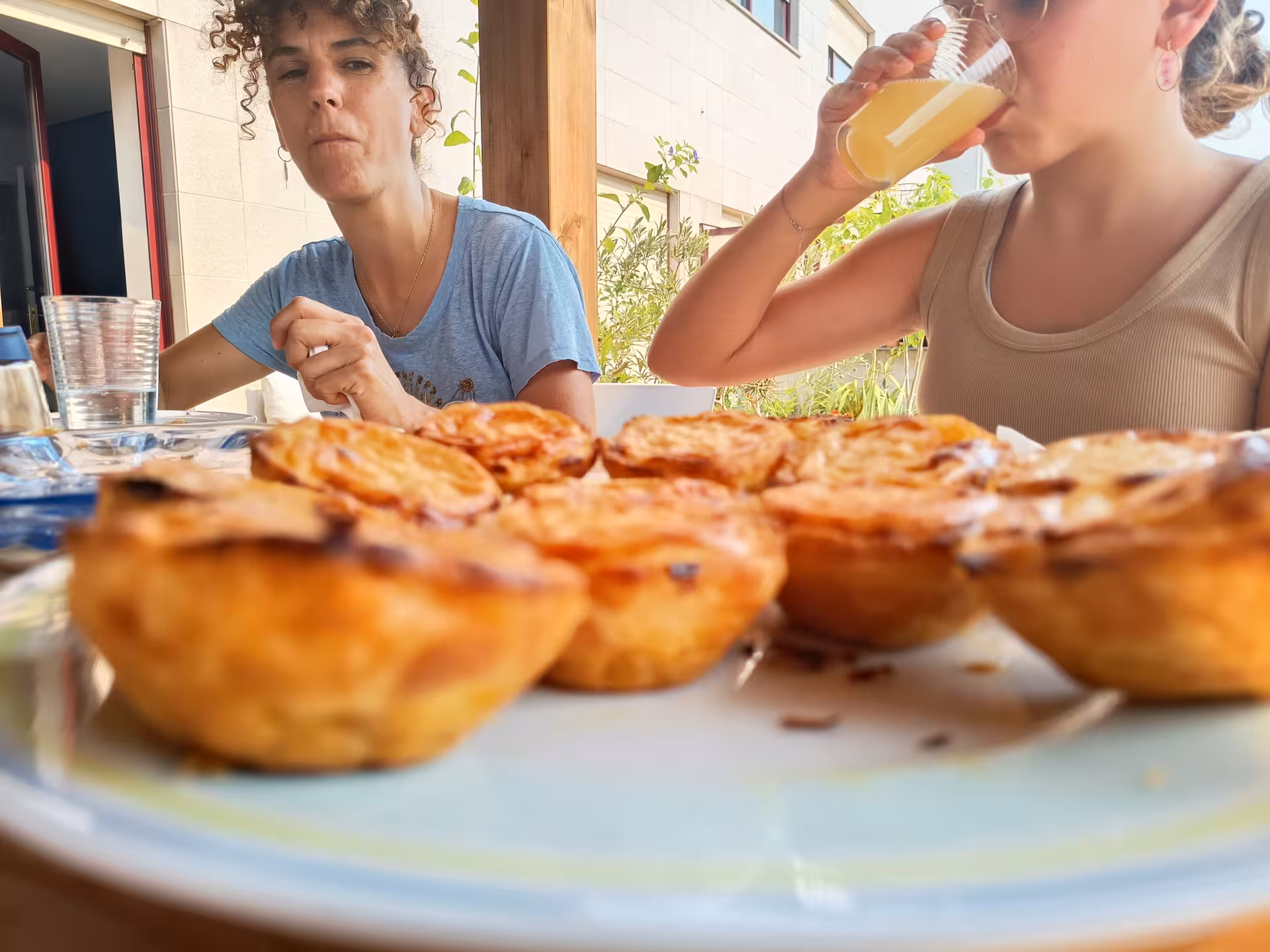 Two people enjoying pastel de nata and juice on a sunny terrace during a cooking class in Portugal.