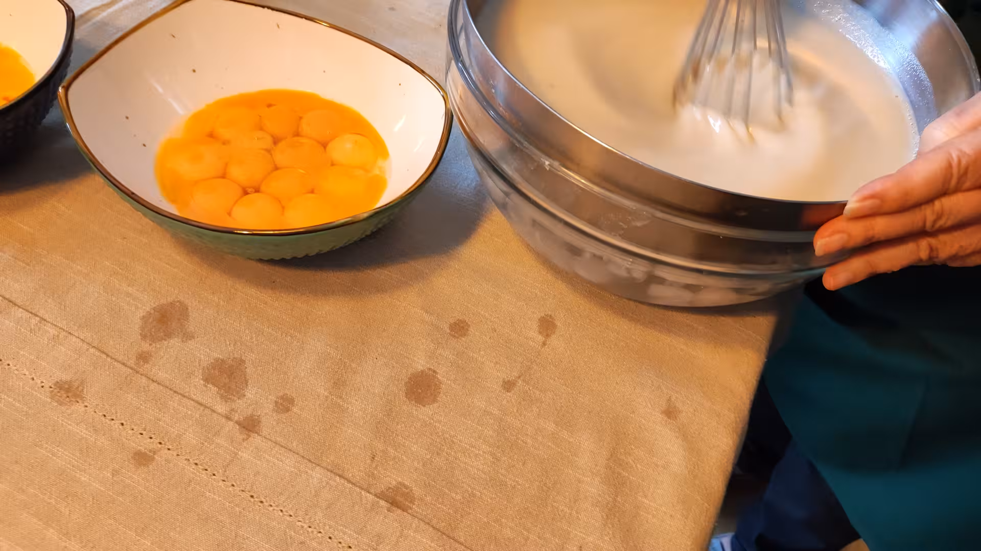 Hands whisking creamy batter beside bowls of egg yolks at Pastel de Nata cooking class on a scenic terrace.
