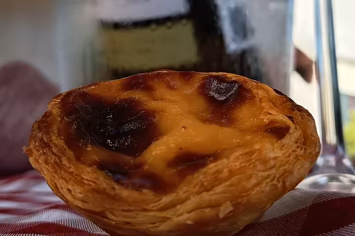 Close-up of a freshly baked Pastel De Nata with a golden crust, set against a rustic tablecloth backdrop.
