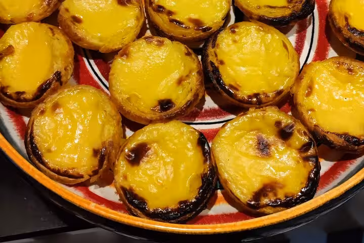 Close-up of freshly baked pastel de nata with golden crusts on a decorative plate, highlighting Portuguese dessert.