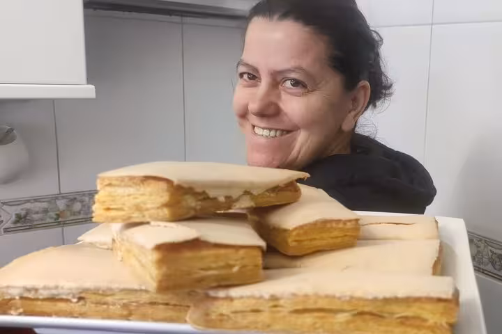 Woman smiling while presenting a plate of traditional Portuguese pastries on a kitchen terrace.