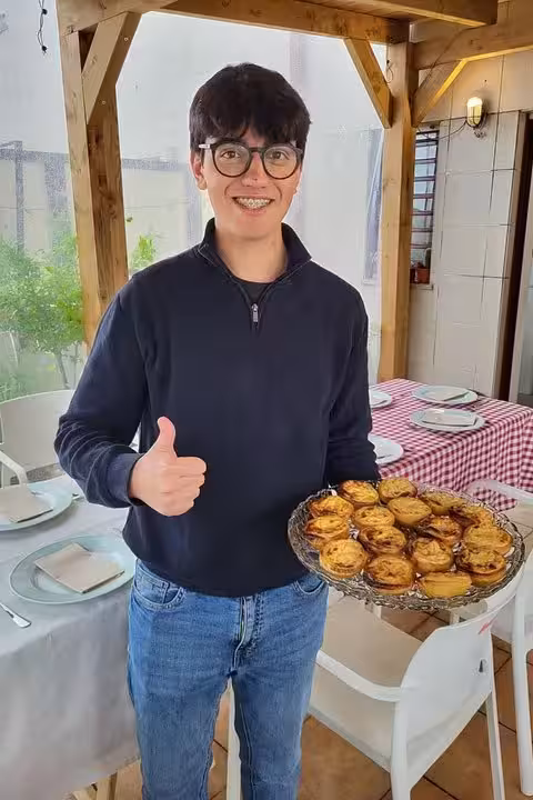 Smiling participant holding a tray of freshly baked pastel de nata on a charming outdoor terrace.