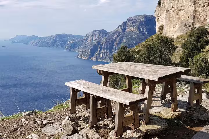 Rustic wooden picnic table overlooking stunning Amalfi Coast vistas on the Path of the Gods hiking trail.