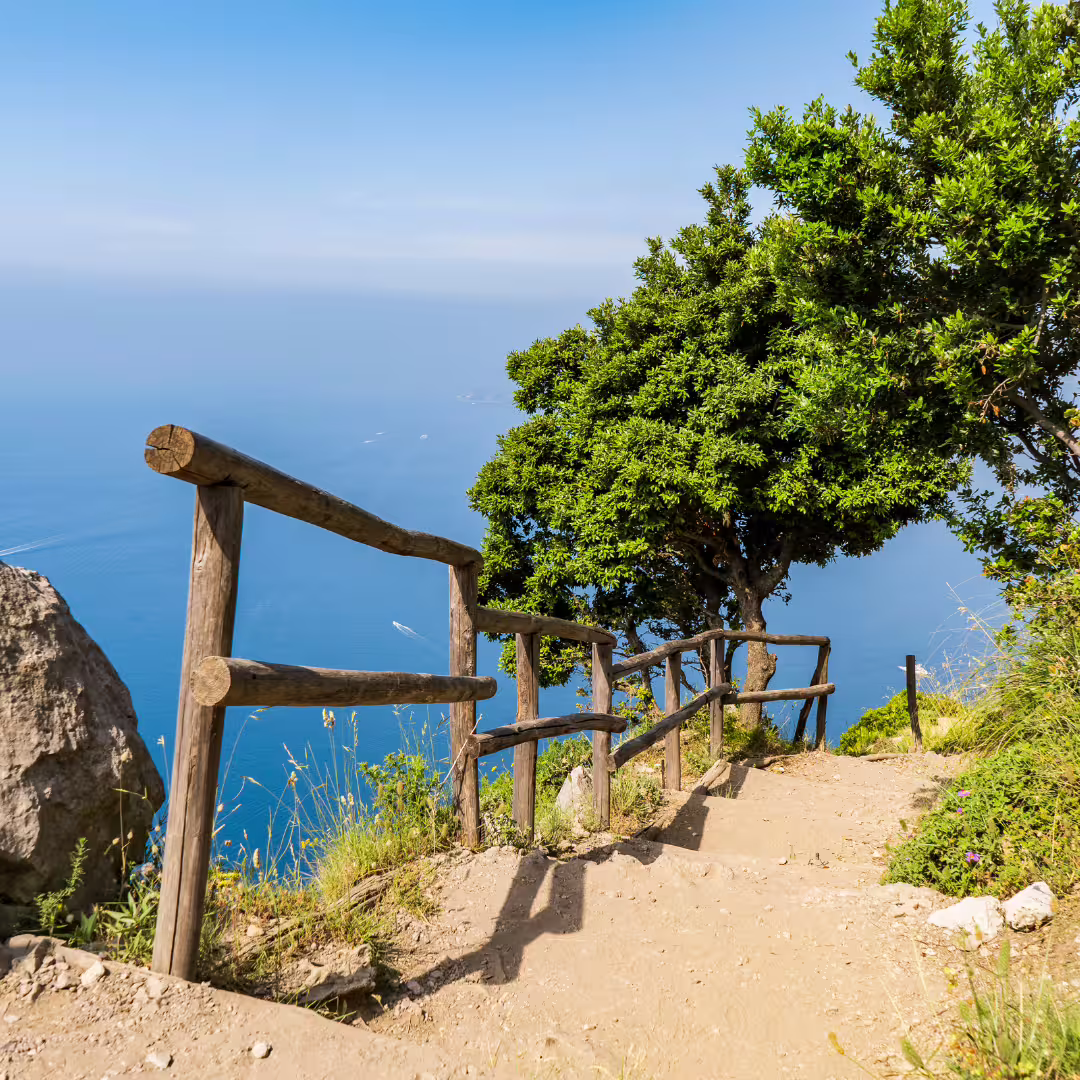 Scenic Path of the Gods trekking trail with rustic wooden railing, coastal cliffs and sweeping Tyrrhenian Sea views