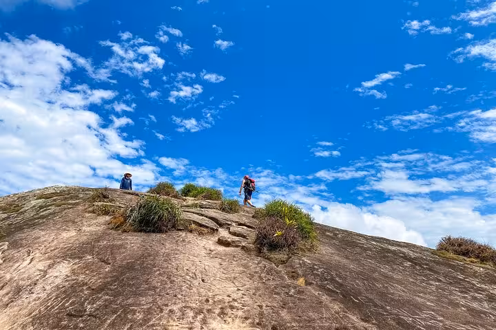 Hikers ascend rocky trail on Peak Sugar Bread under vibrant blue sky, ideal for adventure and nature enthusiasts.