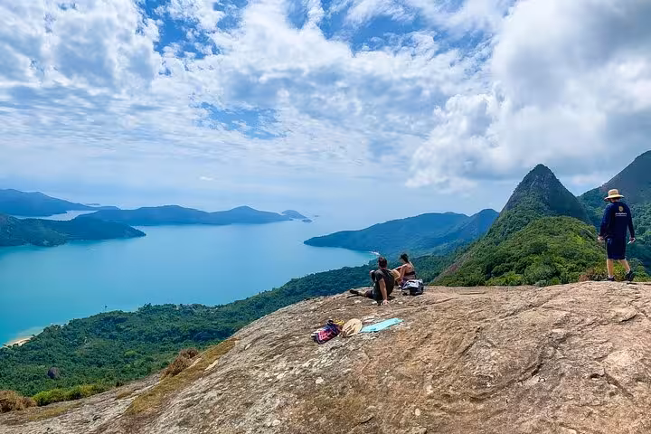 Travelers relax on Peak Sugar Bread's rocky summit, savoring breathtaking vistas of emerald landscapes and azure seas.