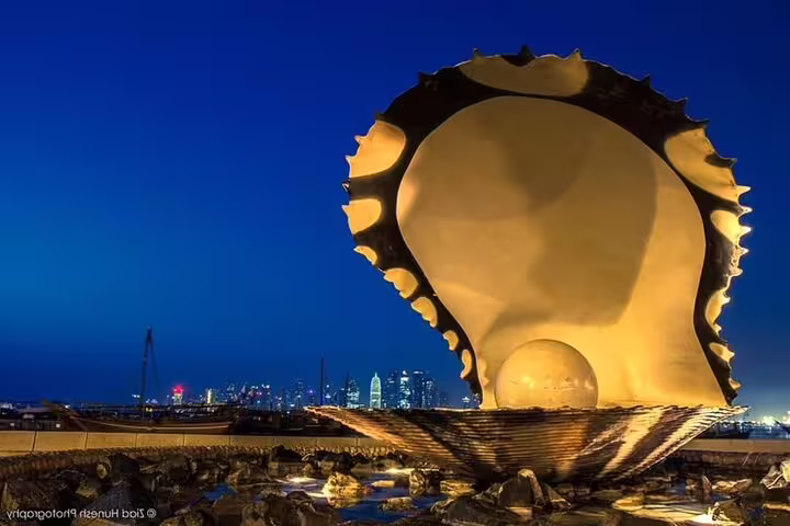 Iconic Pearl Monument at Doha Corniche with city skyline at night, a highlight of the Doha City Tour.
