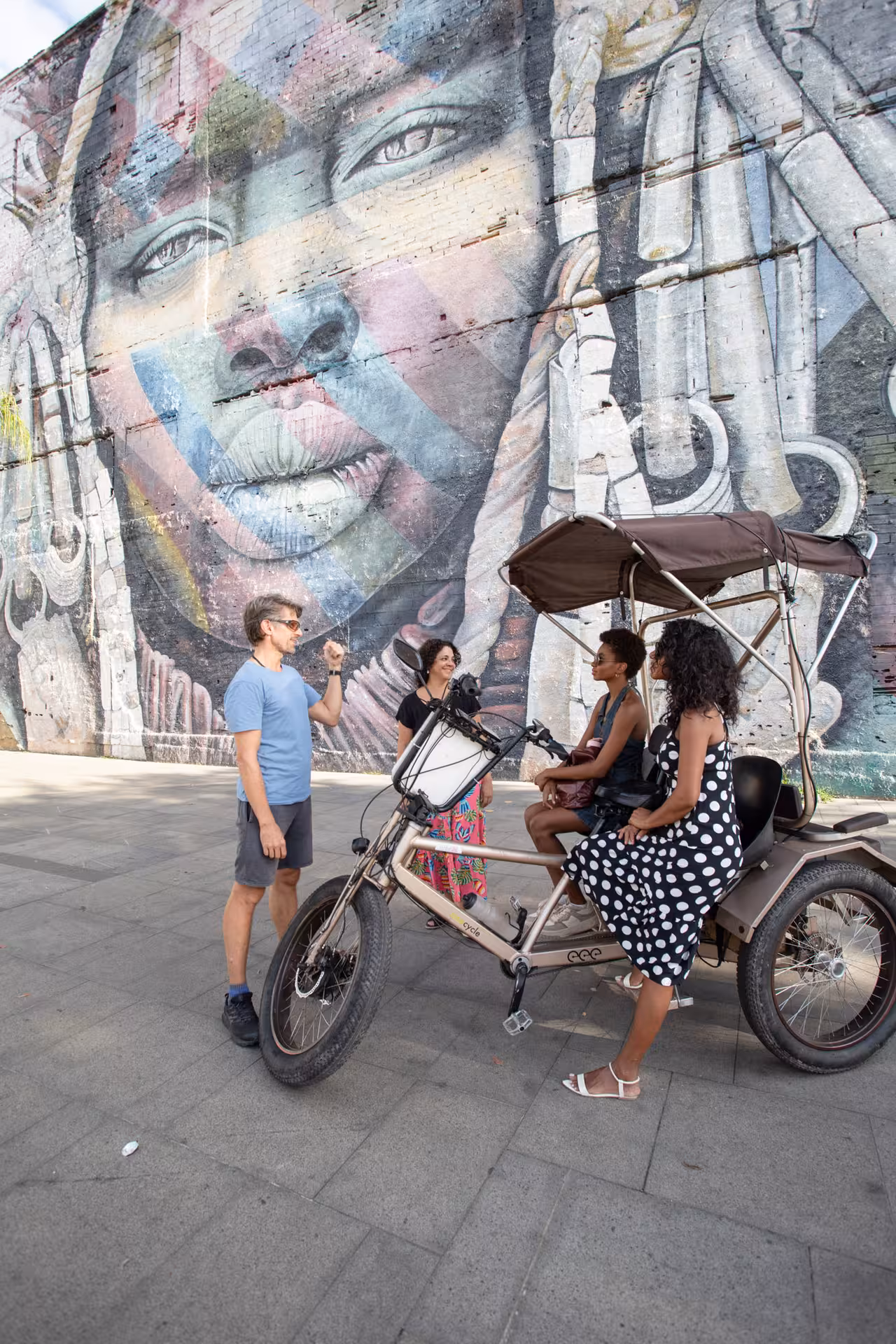 Pedicab tour stops by colorful street art mural in Rio de Janeiro historical city centre, with guide and guests