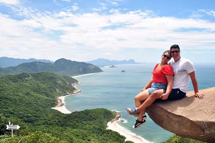Couple enjoys stunning ocean views from Pedra do Telégrafo's famous rock ledge during guided hike in Rio de Janeiro.