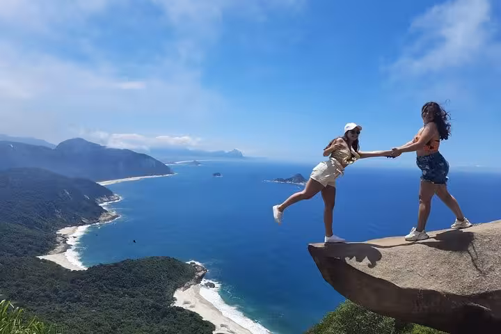Two women experience the thrill of Pedra do Telégrafo's iconic rock ledge, showcasing Rio's scenic hiking adventure.