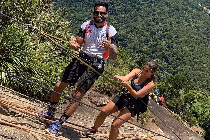 Adventurers scaling the rocky slopes of Pedra da Gávea, harnessed for safety amidst lush Rio forest landscapes.