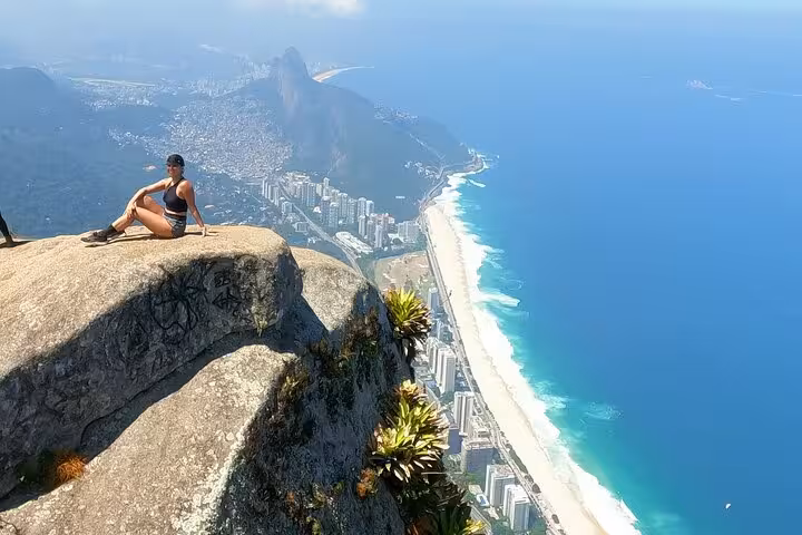 Hiker enjoying breathtaking views from Pedra da Gávea summit overlooking Rio's coastline and lush landscape.
