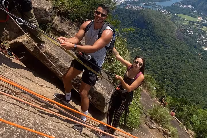 Two hikers climbing Pedra da Gávea, secured with ropes, showcasing thrilling adventure and scenic views in Rio.