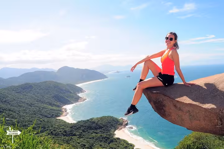 Woman sitting on Pedra do Telégrafo rock, enjoying stunning ocean views during guided hike in Rio de Janeiro.