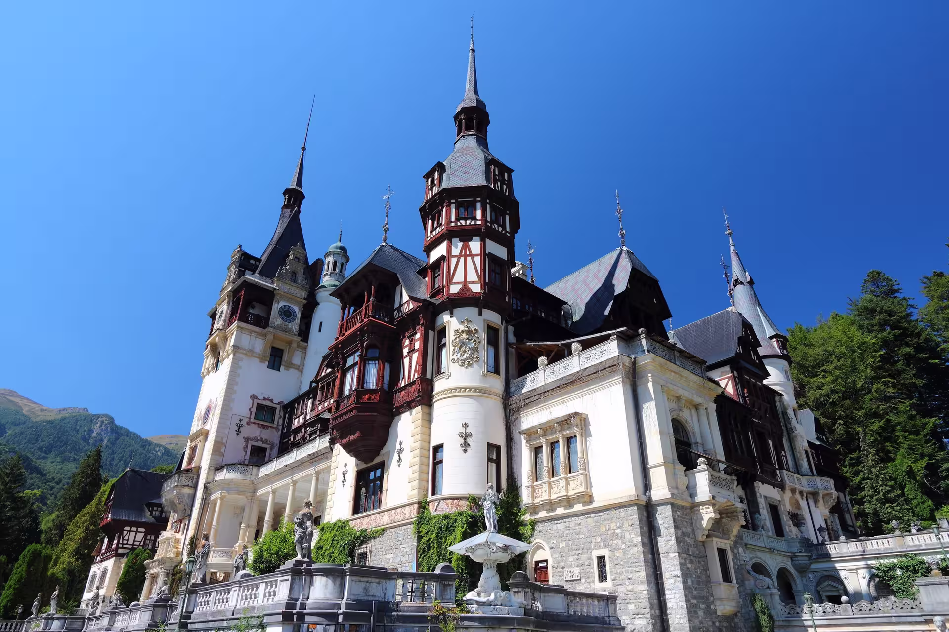 Majestic Peles Castle under a clear blue sky, showcasing its intricate architecture and lush surroundings.
