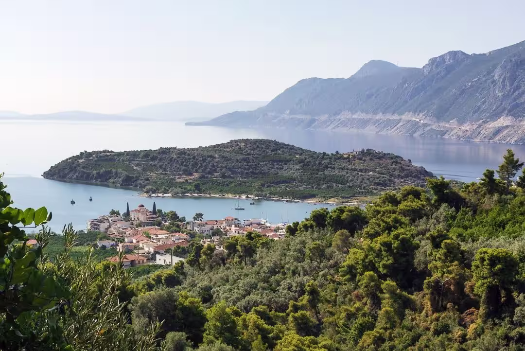 Scenic view of a coastal village in the Peloponnese with lush greenery, mountains, and serene sea, ideal for day trips.