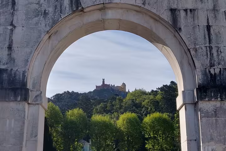 Pena Palace framed through an archway, surrounded by verdant trees, set against a clear sky in Sintra, Portugal.