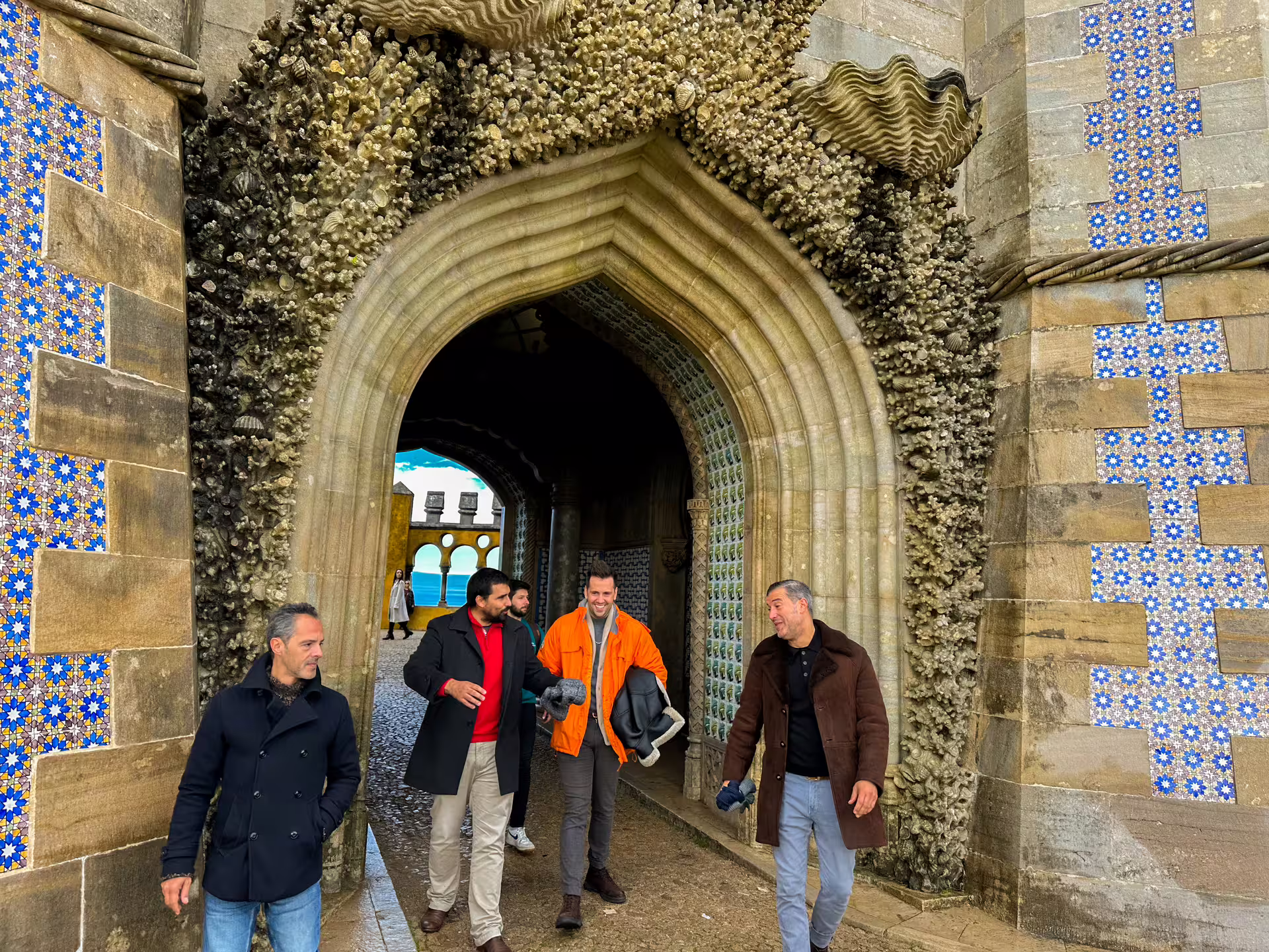 Visitors walking through the ornate archway of Pena Palace, showcasing intricate tiles and stonework on a Sintra van tour.