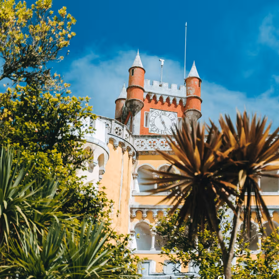 Clock tower and turrets at Pena Palace, Sintra, framed by lush gardens on a Sintra & Cascais day tour