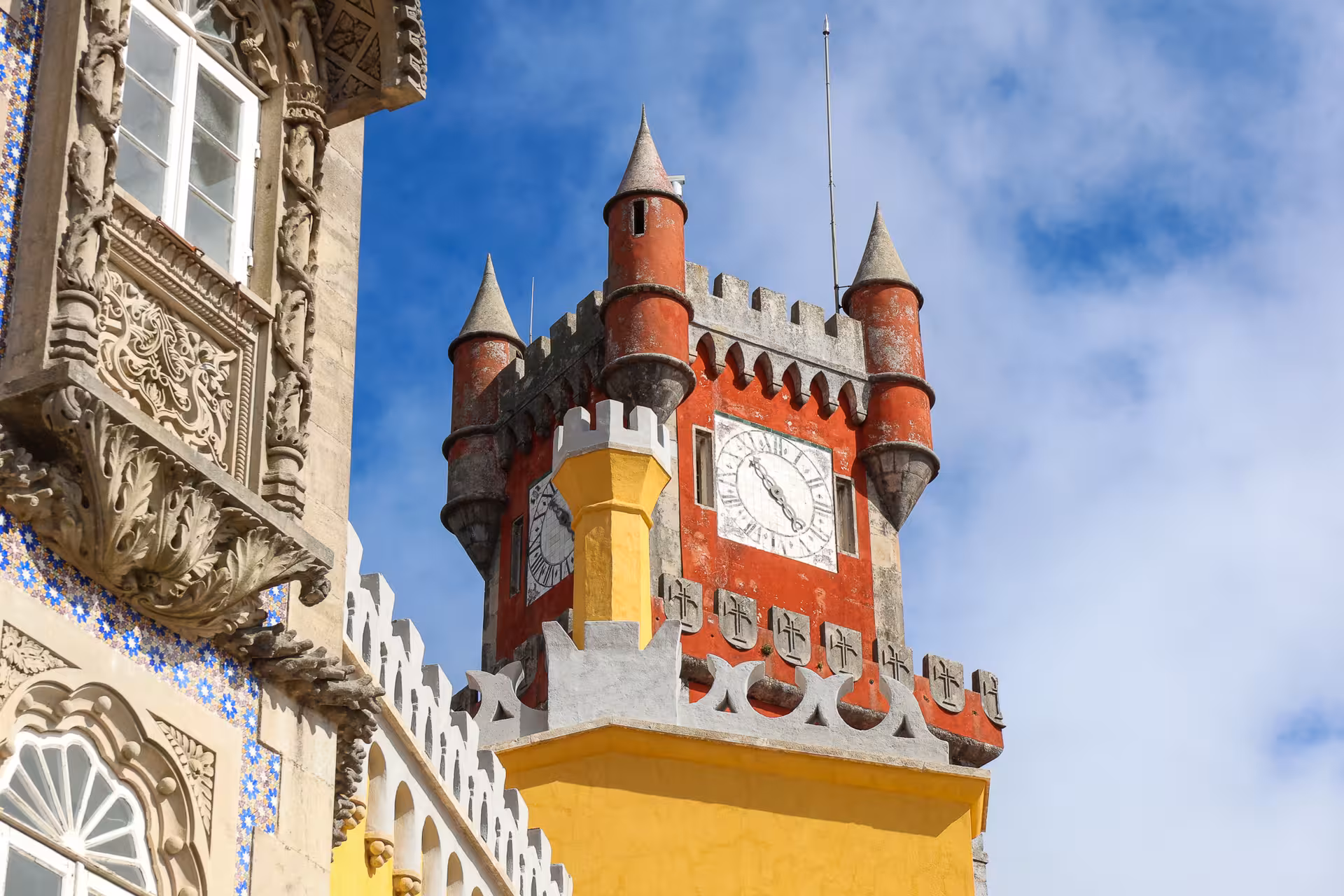 Vibrant red and yellow clock tower of Pena Palace under a bright blue sky in Sintra, Portugal.