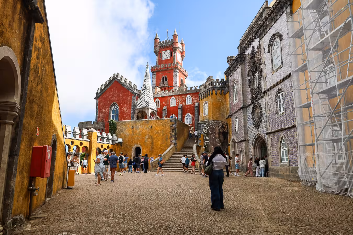 Tourists explore the vibrant and intricate Pena Palace courtyard in Sintra under a bright blue sky.