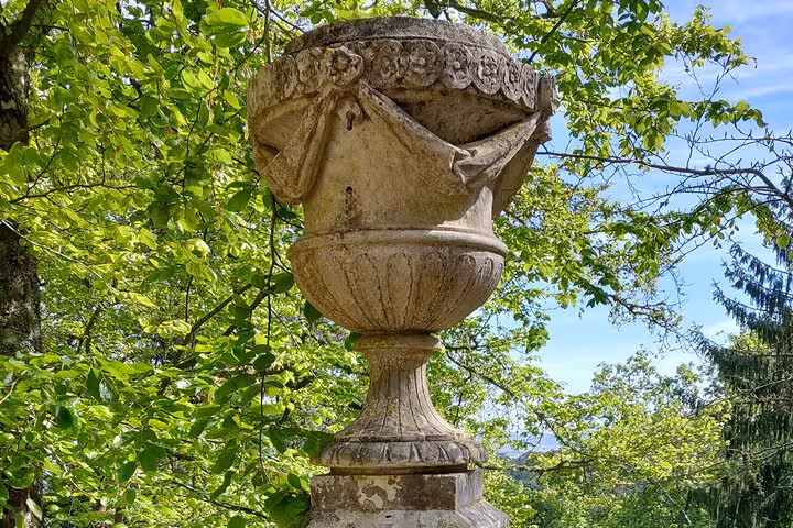 Ornate stone urn amidst lush greenery at Pena Palace gardens, highlighting Sintra's historical charm.