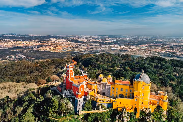 Aerial view of the colorful Pena Palace in Sintra, surrounded by lush greenery, featured in Lisbon's private tour.