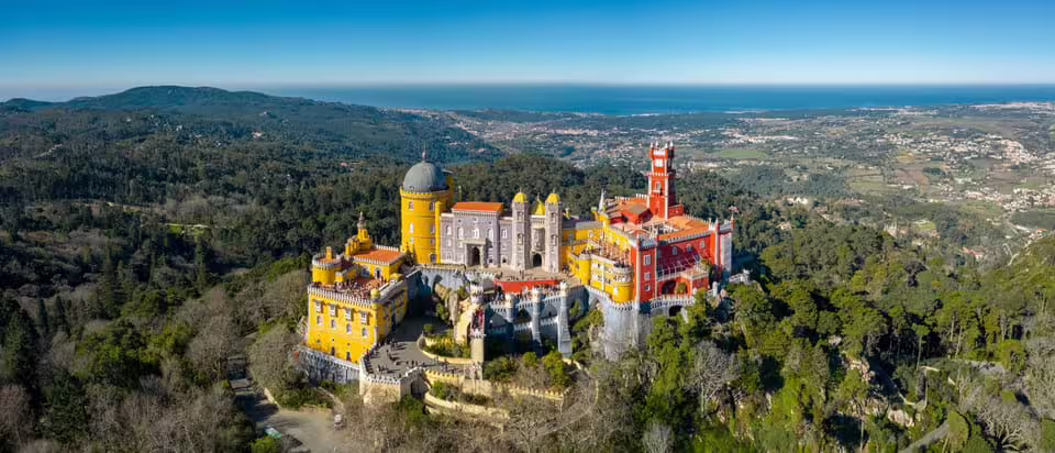 Aerial view of the colorful Pena Palace surrounded by lush greenery in Sintra, a highlight of the full-day tour with tickets.