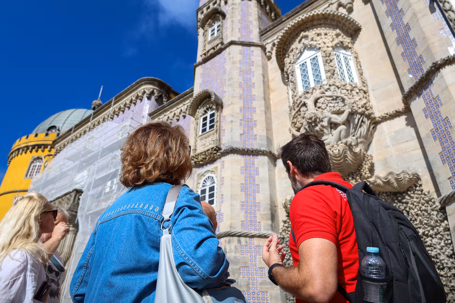 Tourists admiring the intricate architecture of Pena Palace under a clear blue sky in Sintra.