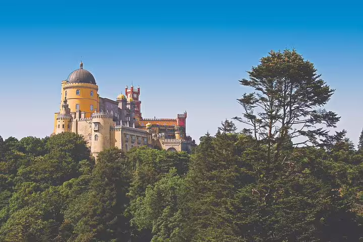 Majestic Pena Palace surrounded by lush greenery under a clear blue sky on the Sintra Cabo da Roca Cascais Estoril tour.
