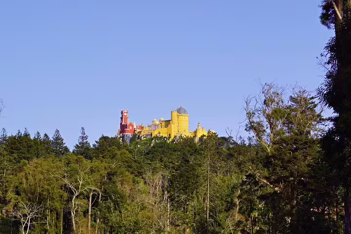 Majestic view of Pena Palace in Sintra, surrounded by lush greenery under a clear blue sky, perfect for a jeep tour.