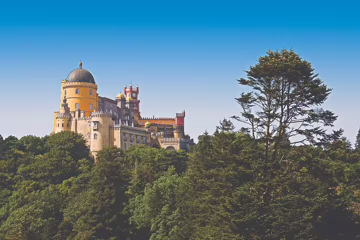 Majestic Pena Palace in Sintra surrounded by lush greenery under a clear blue sky, ideal for a customizable private day tour.