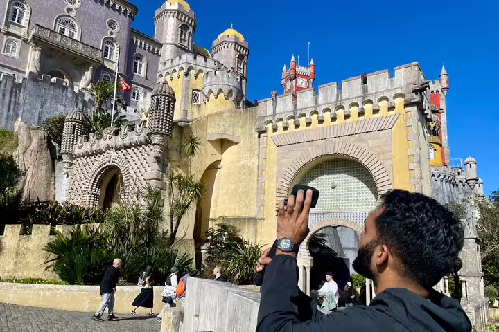 Traveler admires the vibrant architecture of Pena Palace on a sunny day during the Sintra & Cascais Hidden Gems Tour.