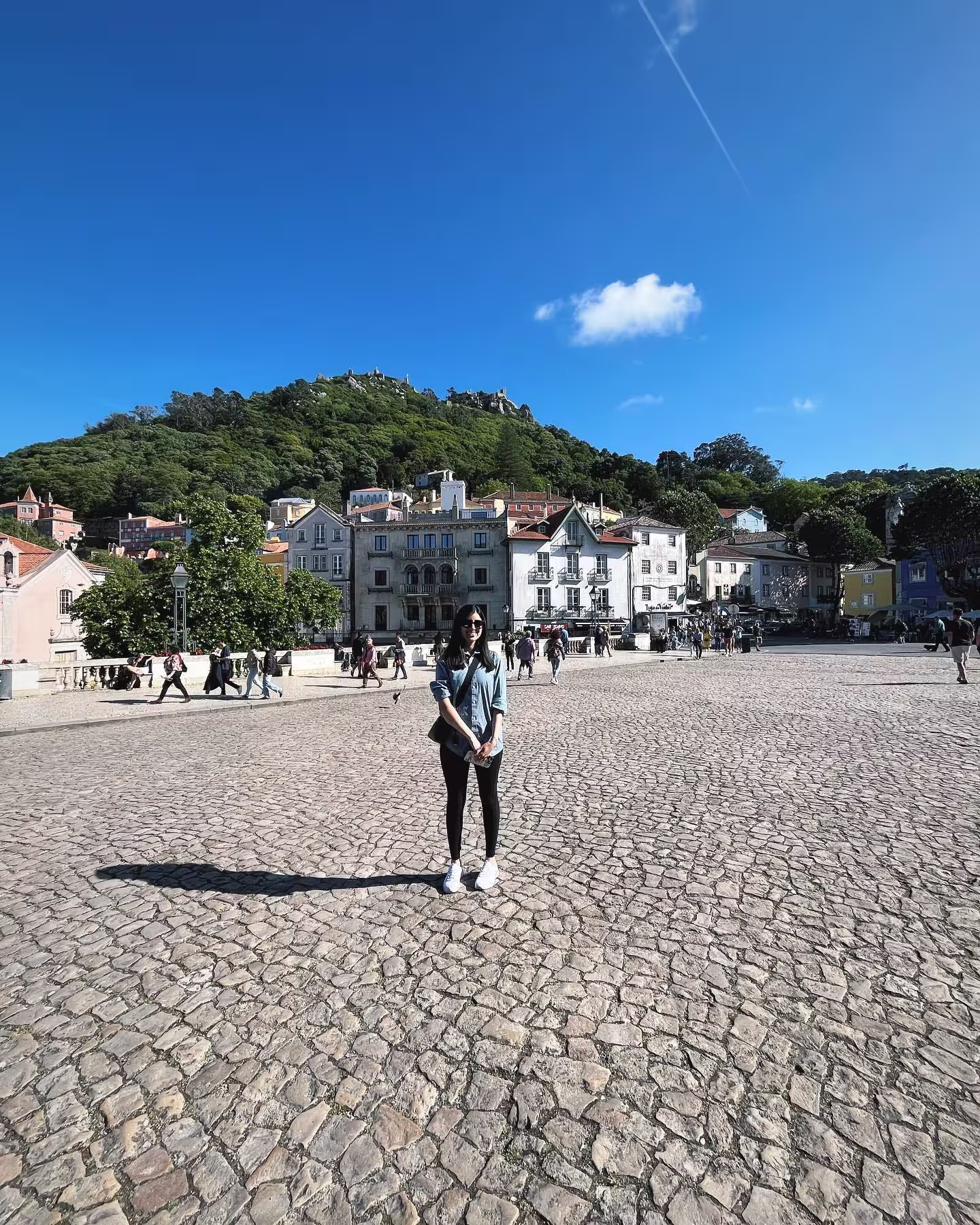 Visitor standing in a cobblestone square with historic buildings and lush hilltop views in the heart of Sintra.