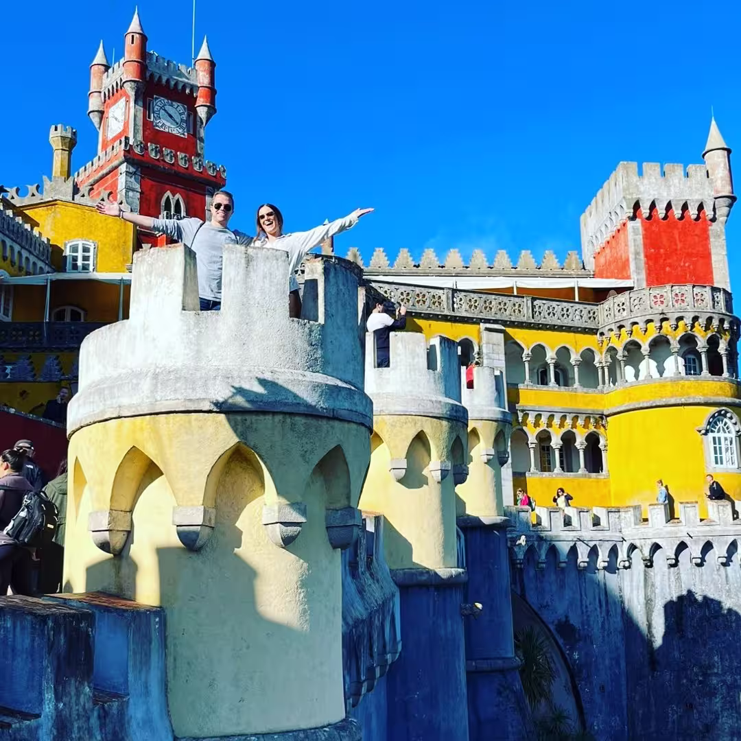 Visitors enjoying the vibrant, colorful architecture of Pena Palace in Sintra under a clear blue sky.