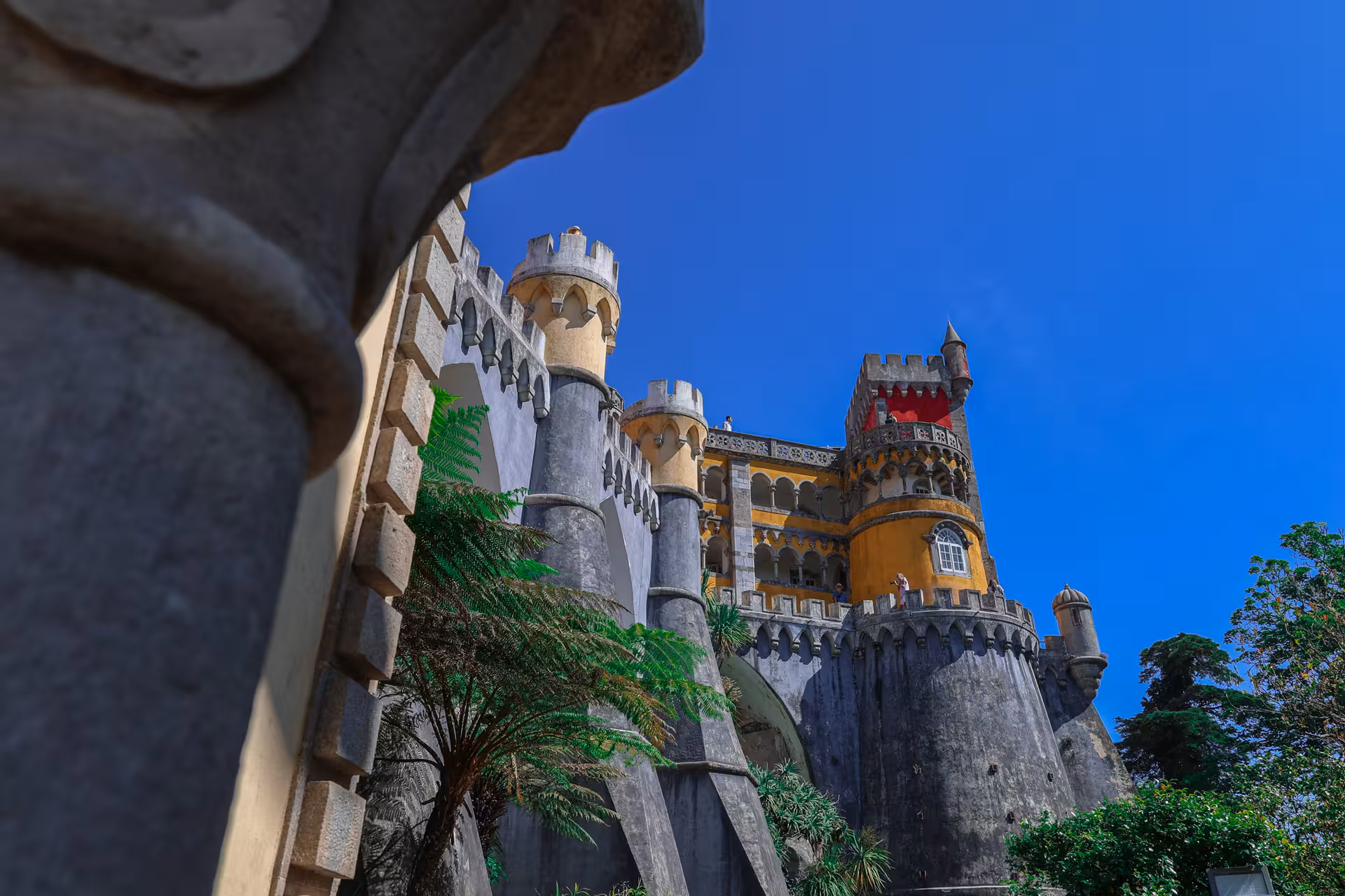 Vibrant Pena Palace in Sintra under a clear blue sky, showcasing its colorful architecture and lush surroundings.