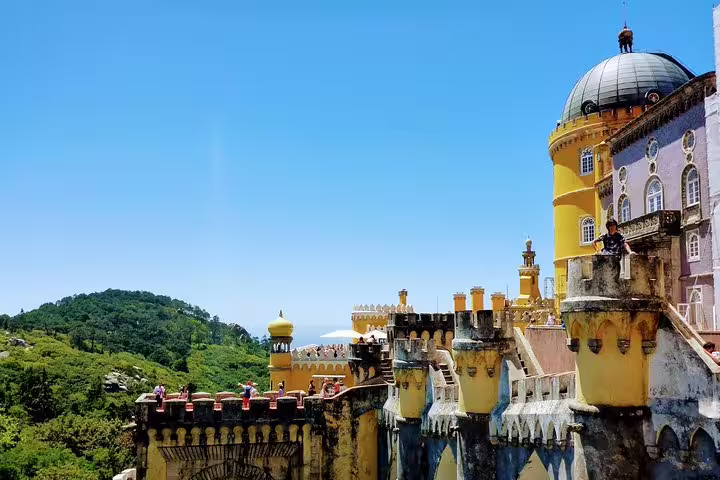 Colorful view of Pena Palace in Sintra on a sunny day, highlighting the vibrant architecture and lush surrounding landscape.