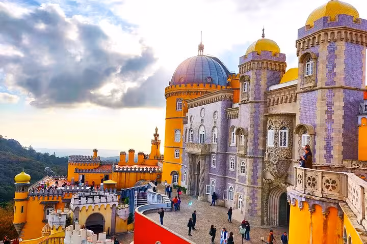 Colorful and majestic Pena Palace in Sintra with tourists exploring its vibrant exterior under a dramatic sky.