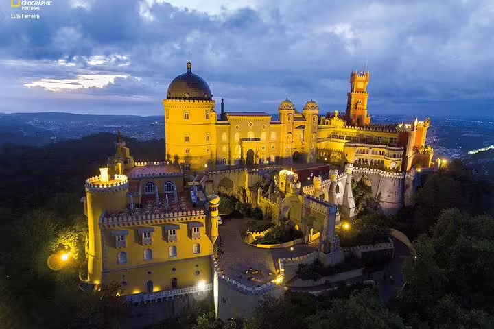 Stunning evening view of Pena Palace in Sintra, Portugal, illuminated against a dramatic sky, featured on private tour itineraries.