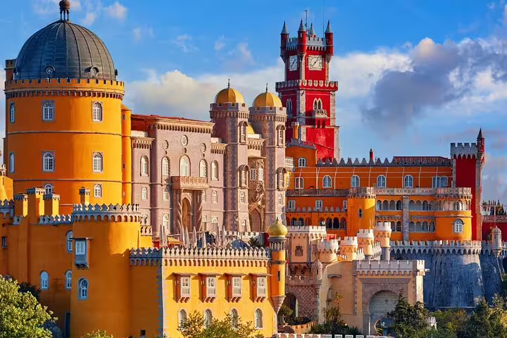 Vibrant view of Pena Palace in Sintra with colorful turrets against a blue sky, featured in a full-day tour including Cabo da Roca and Cascais.