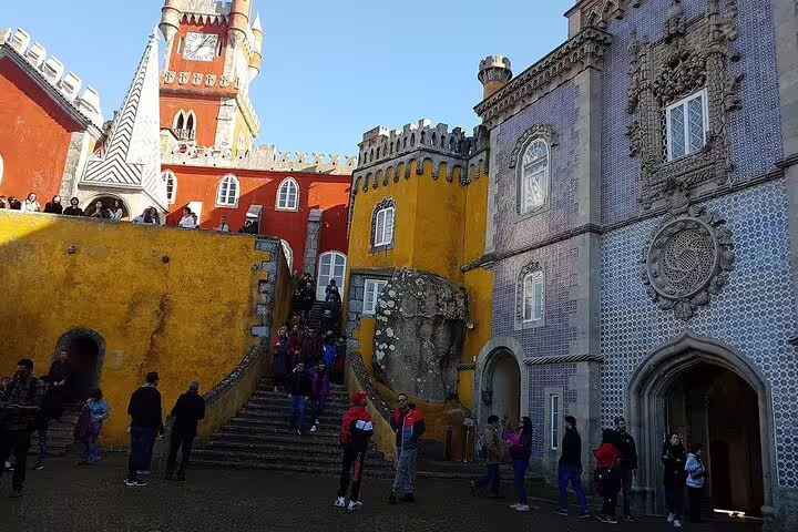 Visitors explore the vibrant architecture of Pena Palace in Sintra on a scenic day trip from Lisbon, including Cabo da Roca and Cascais.