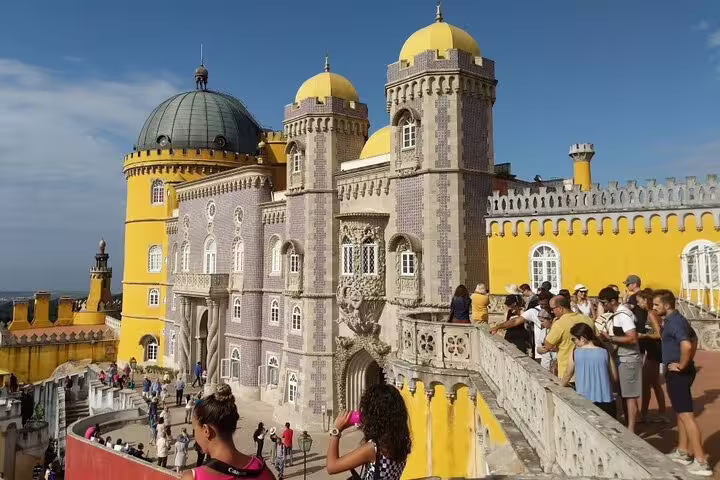 Tourists explore the vibrant architecture of Pena Palace in Sintra on a sunny day, part of a Lisbon to Cascais day trip.