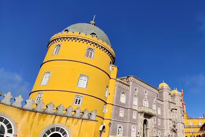 Vibrant yellow and gray facade of Pena Palace in Sintra, Portugal, under a clear blue sky, featured in our Lisbon day trip.
