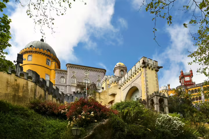 Vibrant facade of Pena Palace in Sintra, Portugal, surrounded by lush gardens under a bright blue sky.