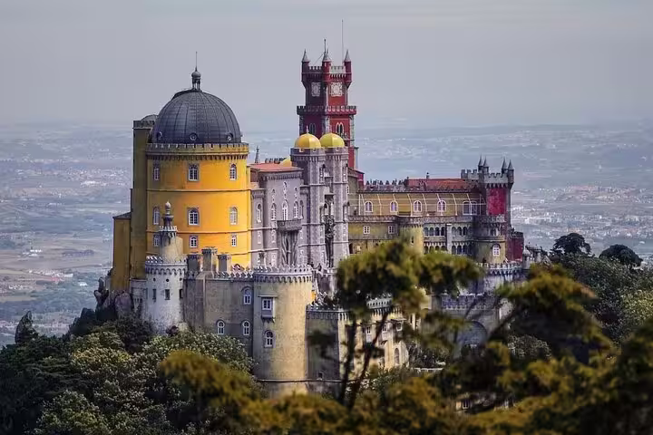 Vibrant view of Pena Palace in Sintra, Portugal, showcasing its colorful architecture amidst lush greenery on a private half-day tour.