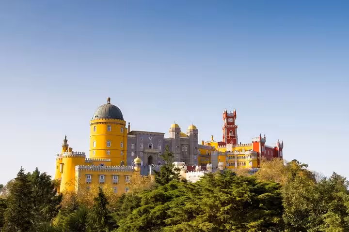 Vibrant Pena Palace perched atop a hill surrounded by lush greenery in Sintra, Portugal, under a clear blue sky.