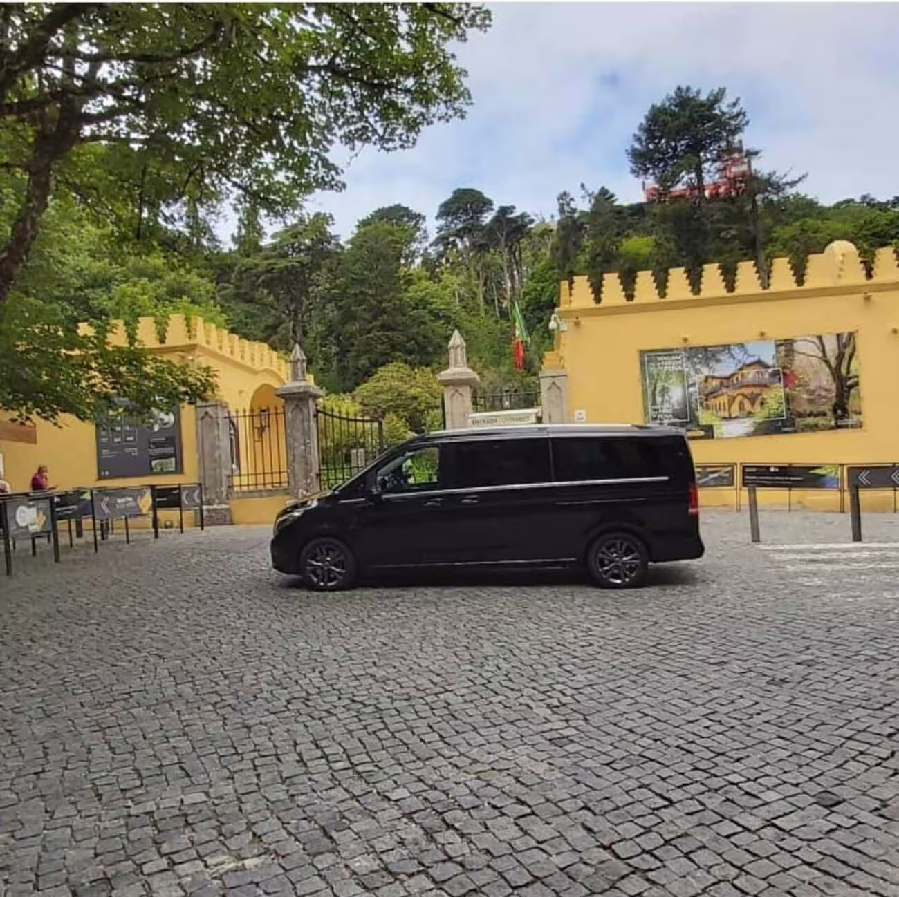 Black van parked outside the entrance of Pena Palace, surrounded by lush greenery in Sintra, Portugal.