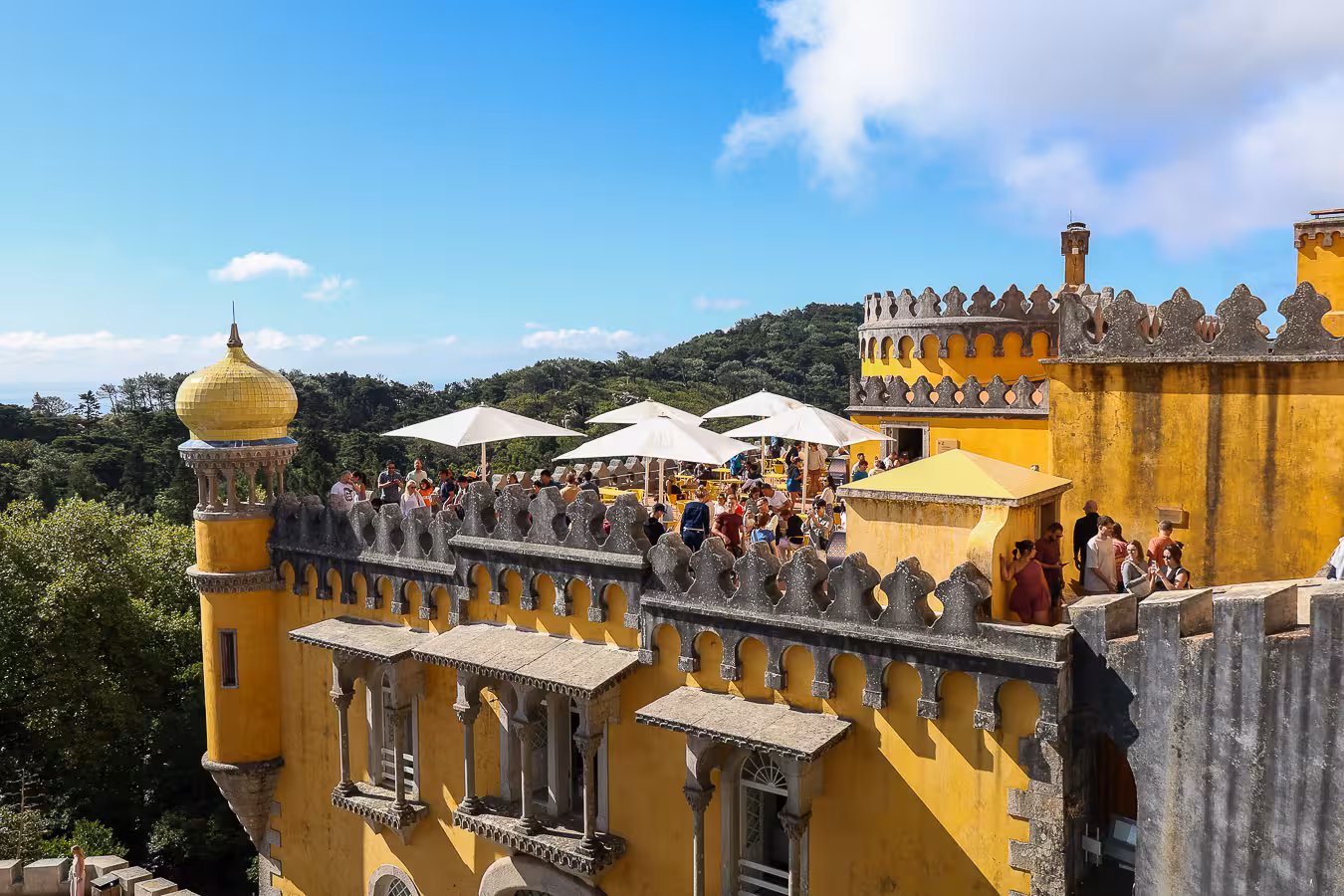 A sunny day at Pena Palace in Sintra with tourists enjoying panoramic views from the terrace and iconic yellow domes.