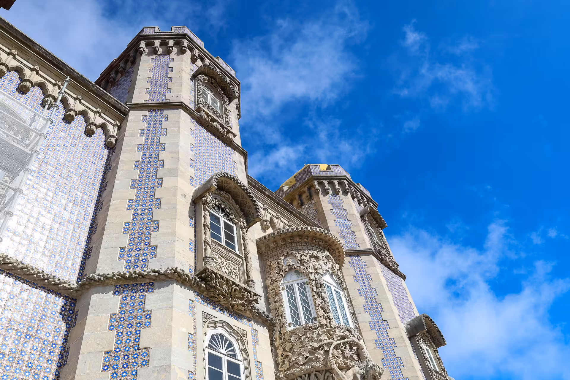 Intricate tilework and ornate windows of Pena Palace's facade against a bright blue sky in Sintra, Portugal.