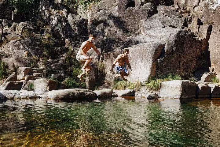Adventurers jumping into a crystal-clear lagoon at Peneda Geres National Park during a private tour from Porto.